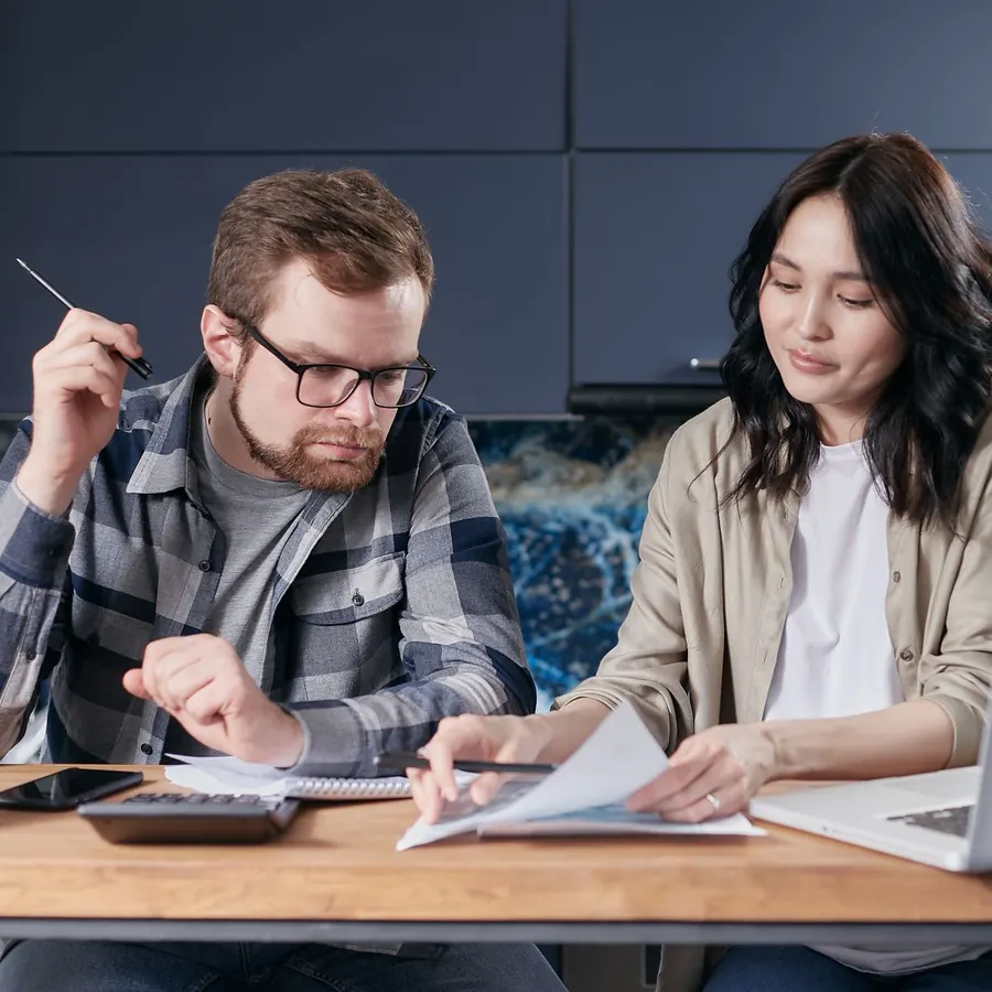 Two people reviewing documents with a calculator and laptop